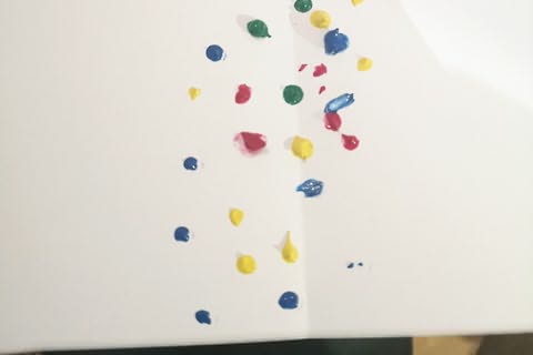 Folha de papel com vinco a meio e várias gotas de tintas coloridas dispostas ao acaso