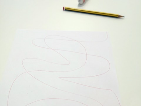 Folha de papel riscada com linha sinuosa; atrás, um lápis e borracha