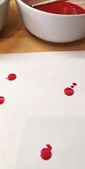 Uma tigela com tinta vermelha e uma folha de papel com várias gotas de tinta