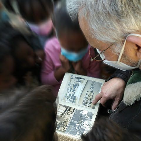 Crianças rodeando adulto segurando livro de fotografias antigas aberto