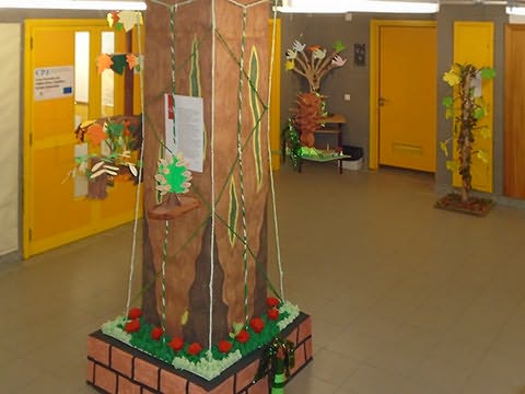 Átrio com coluna a meio forrada a papel pintado como um tronco de árvore e 3 árvores de papel com folhas coloridas em fundo.