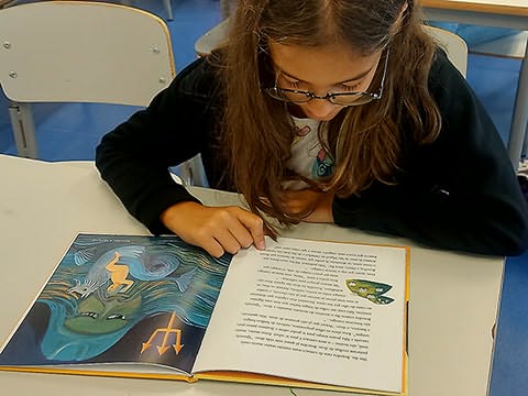 Menina de óculos sentada em secretária lendo livro