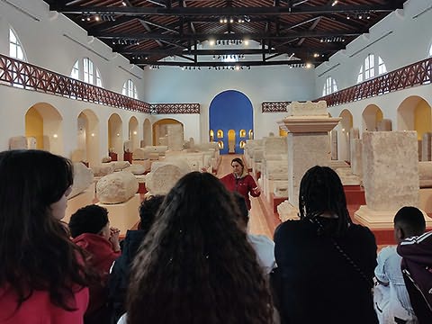 Alunos observando grande sala com restos de colunas e várias pedras inscritas