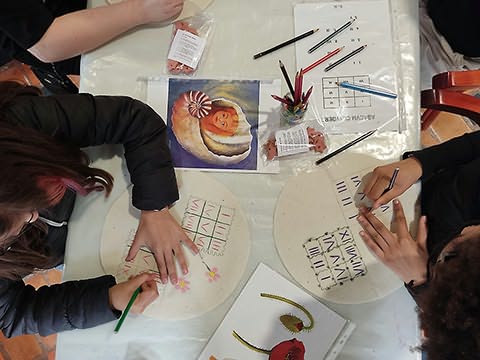 Dois alunos vistos de cima desenhando e escrevendo em panos com quadrículas de 3 por 3