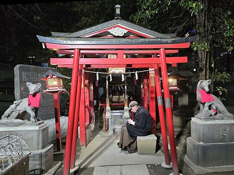 P&oacute;rticos de estilo oriental vermelhos, ao lado est&aacute;tuas de animais em pedestal e uma pessoa sentada &agrave; entrada