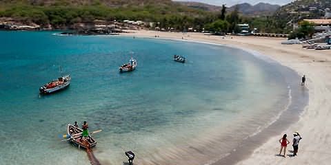 Praia de areias claras e água turquesa com pequenos barcos