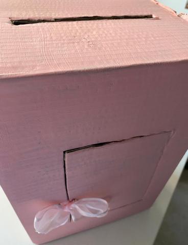 Caixa de cartão com ranhura no topo e porta recortada na lateral com laço de seda cor-de-rosa
