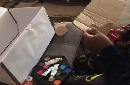 Menino recortando cartão, paleta com guaches e caixa de sapatos forrada a papel branco