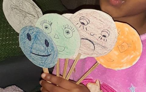 Menina segura fantoches de emoções de cores várias realizados em cartão e pauzinhos chineses