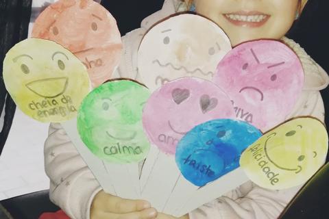 Menina com fantoches de emoções realizados com caras de cartão pintadas a aguarela de cores várias e suportes de cartão